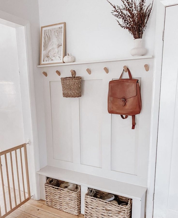 a white bench with baskets on it next to a wall mounted coat rack and door