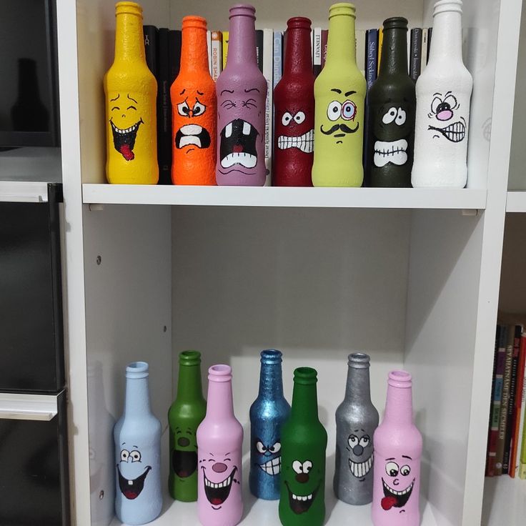 many different colored bottles with faces painted on them in a white shelf next to books