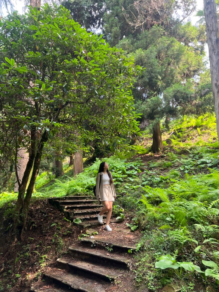 a woman is walking up some steps in the woods with trees and plants on either side