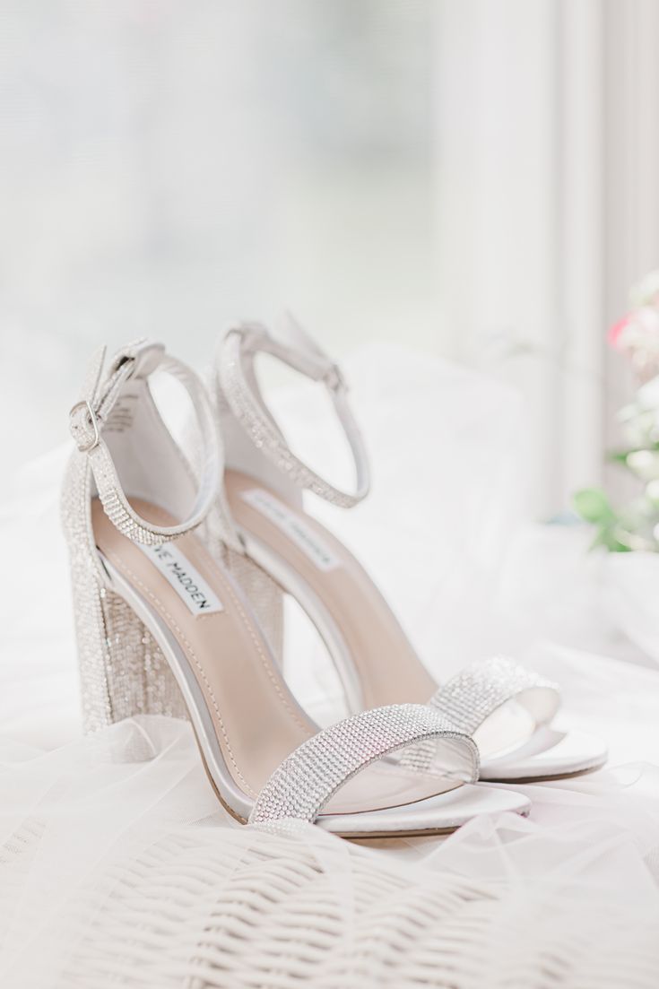 a pair of white high heel shoes on top of a bed with flowers in the background