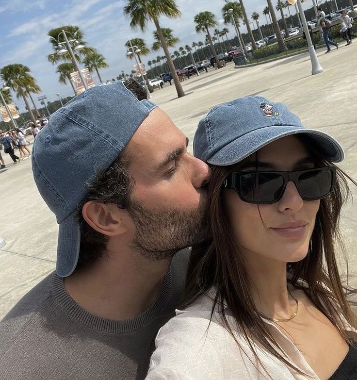 a man and woman kissing each other in front of palm trees on a sunny day