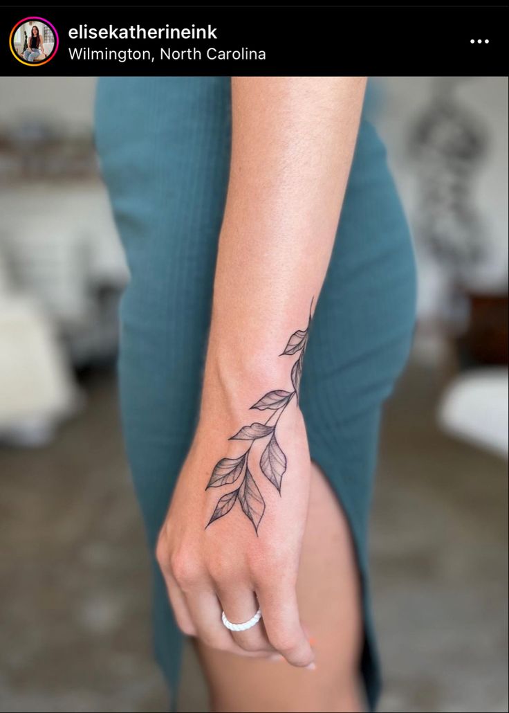 a woman's hand with a small leaf tattoo on her left wrist and the other arm behind her