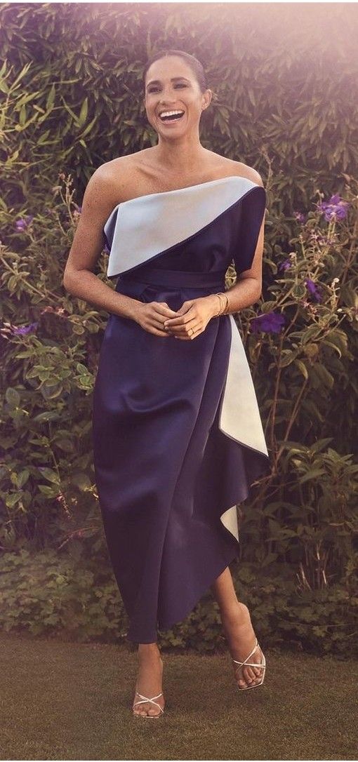 a woman in a blue and white dress standing next to a bush with purple flowers