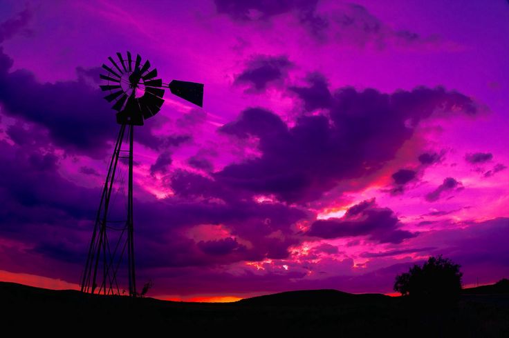 a windmill sitting in the middle of a field under a purple and pink sky with clouds