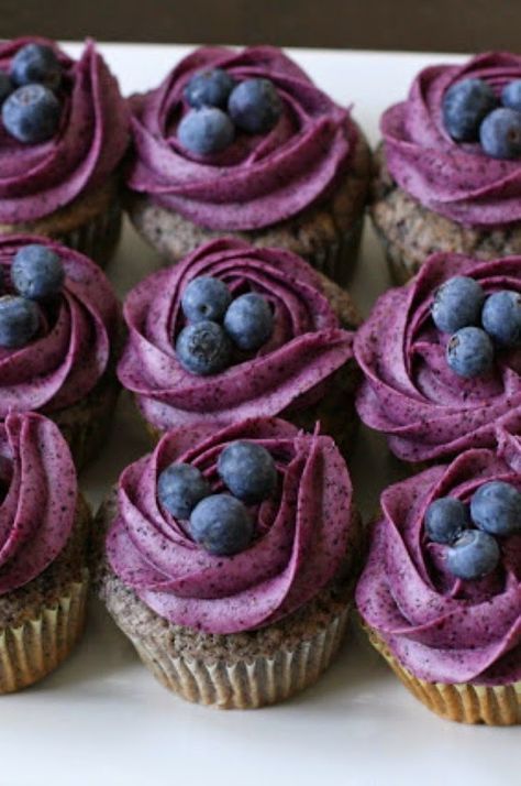 cupcakes with purple frosting and blueberries are on a white platter