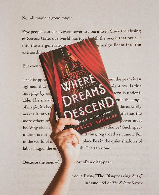 a hand holding up a book in front of an open page with the title where dreams descend