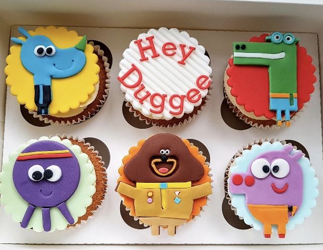 cupcakes decorated to look like cartoon characters are in a box with the words hey dugge on them