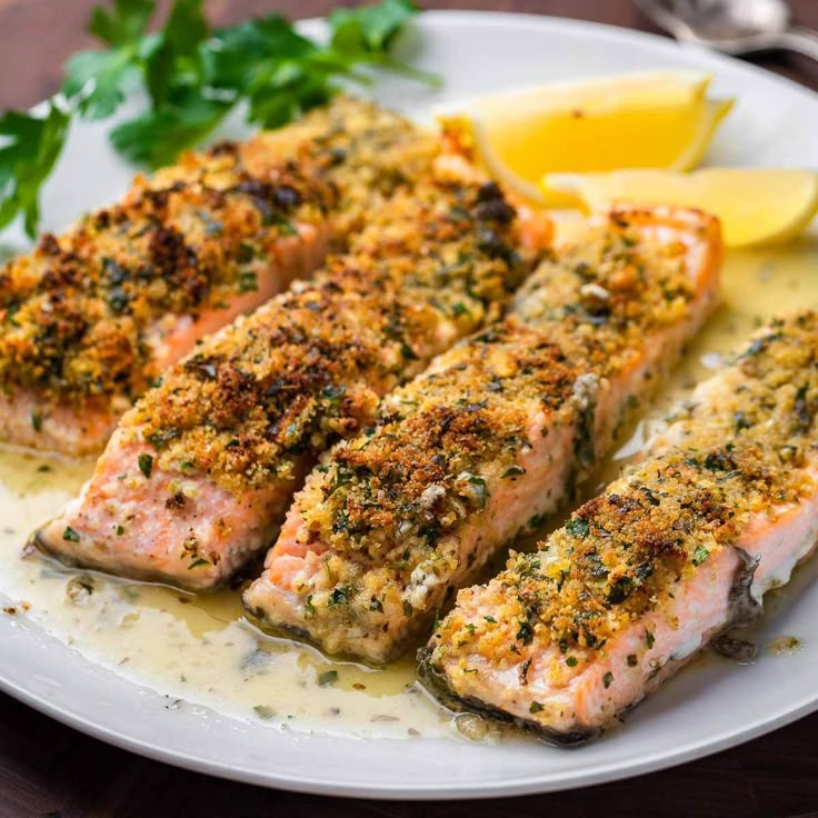 two salmon fillets on a plate with lemon wedges and parsley garnish