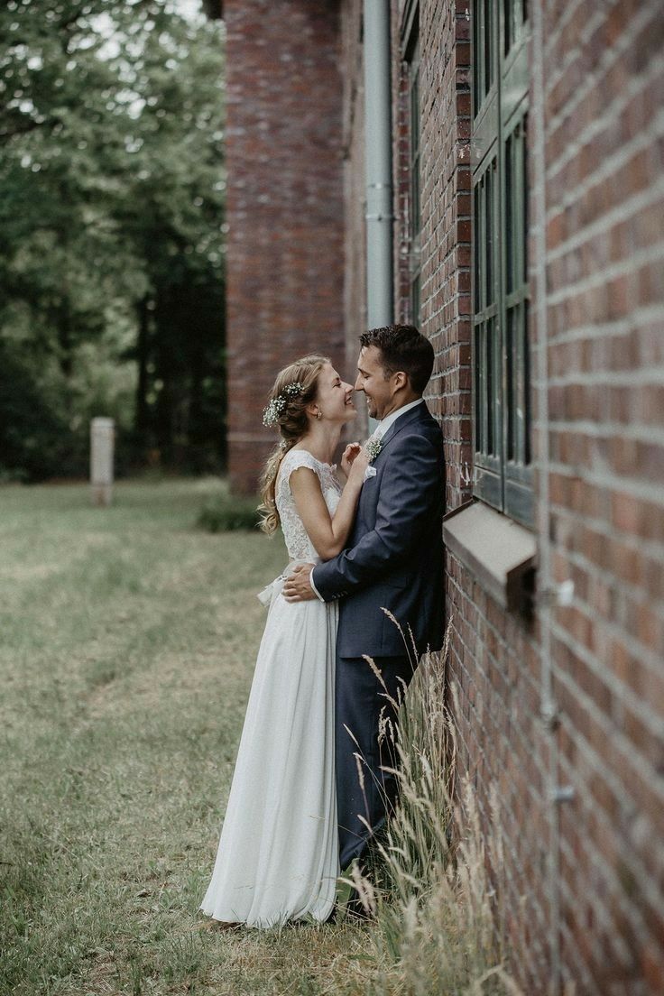 a bride and groom leaning against a brick wall in front of an old building kissing