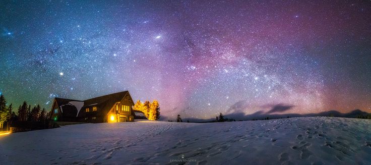 the night sky is filled with stars and bright lights above a cabin on a snowy hill