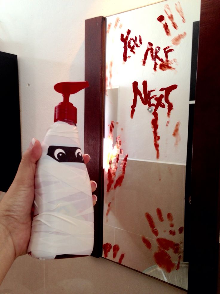 a hand holding a bottle with red paint on it in front of a mirror that says you are not