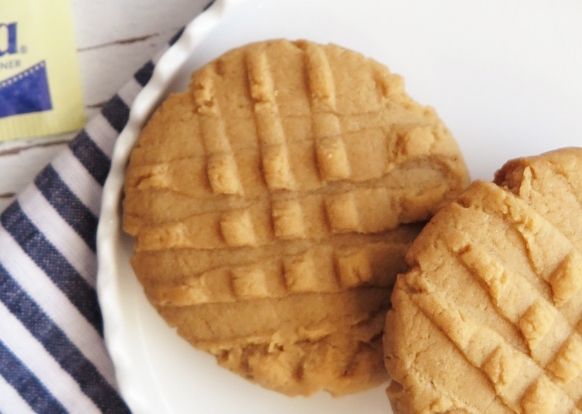 two peanut butter cookies on a plate next to a bottle of milk and a striped towel