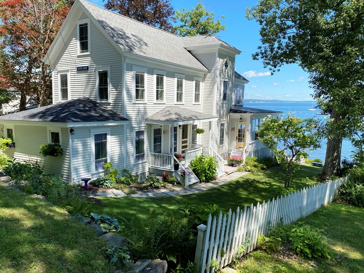 a large white house sitting on top of a lush green field next to the ocean