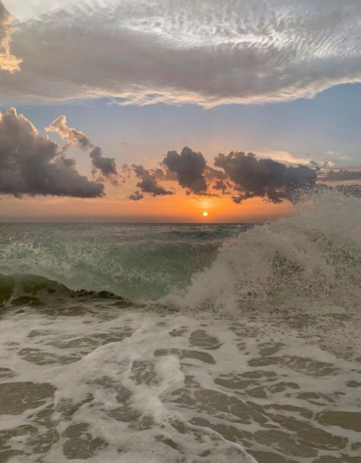 the sun is setting over the ocean with waves crashing on the shore and clouds in the sky