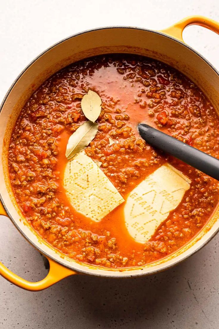 a pot filled with chili and cheese on top of a white counter next to a wooden spoon