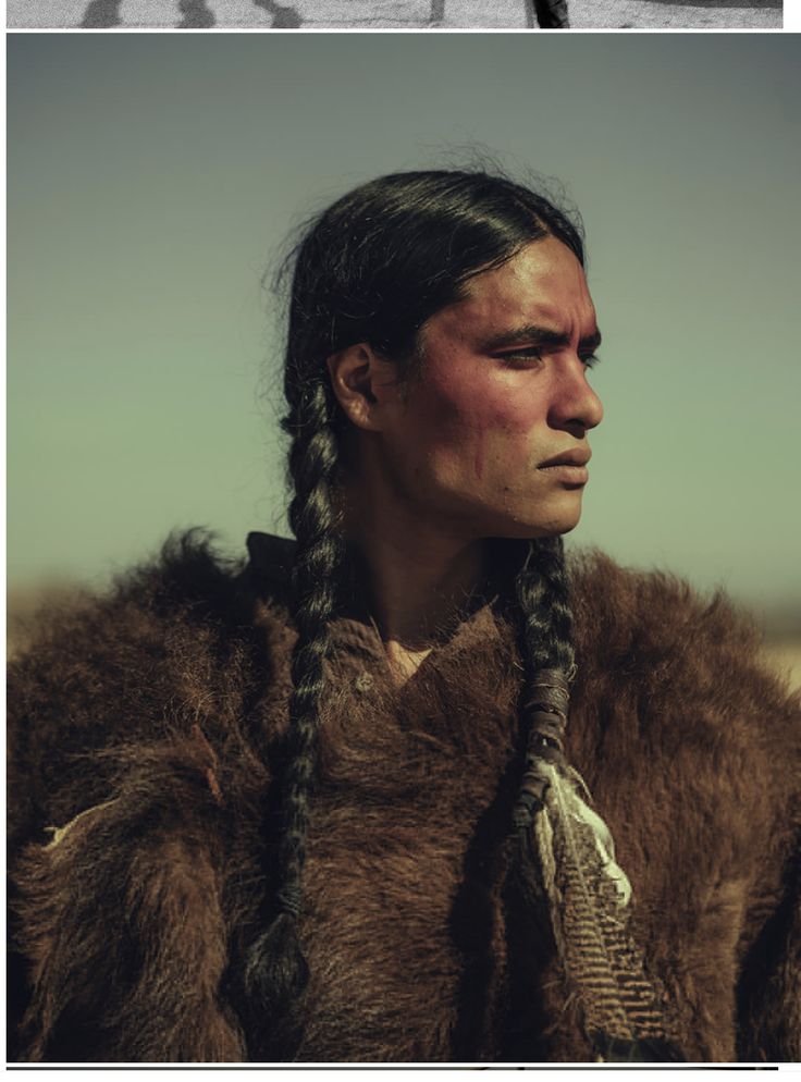 a man with long hair and braids in a fur coat looking off into the distance