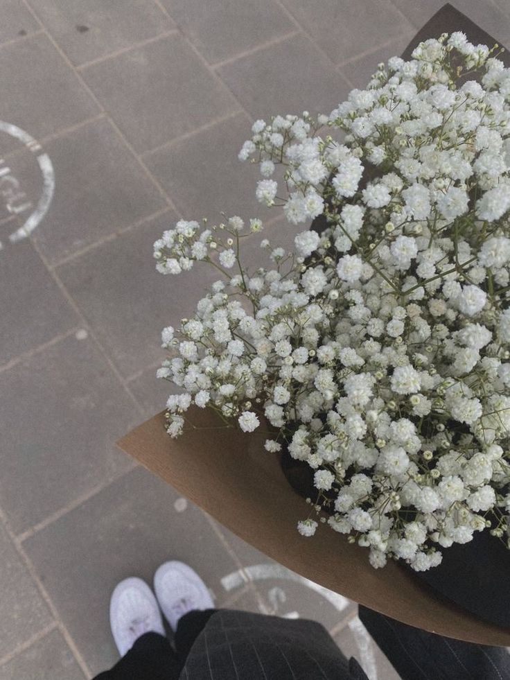 a bouquet of white flowers sitting on top of a wooden table next to someone's feet