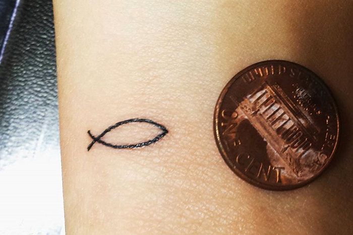 a penny sitting next to a small fish tattoo on the side of a woman's arm