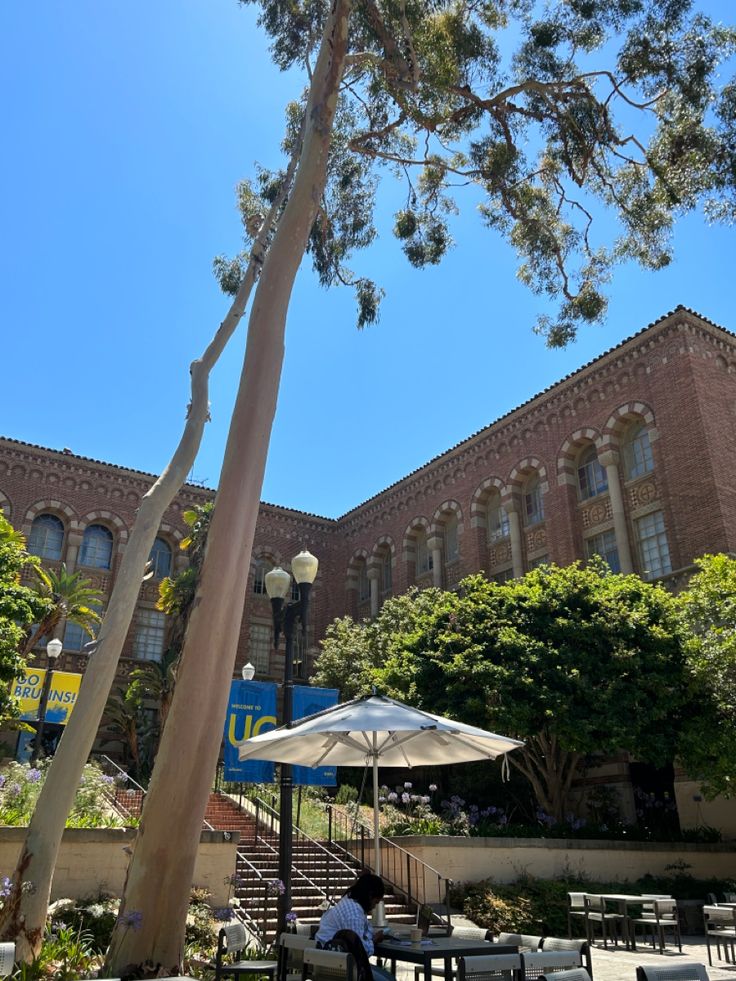 a person sitting at a table under an umbrella in front of a large brick building