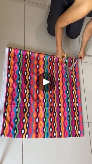 a person is cutting up a colorful piece of fabric on the floor with scissors and tape