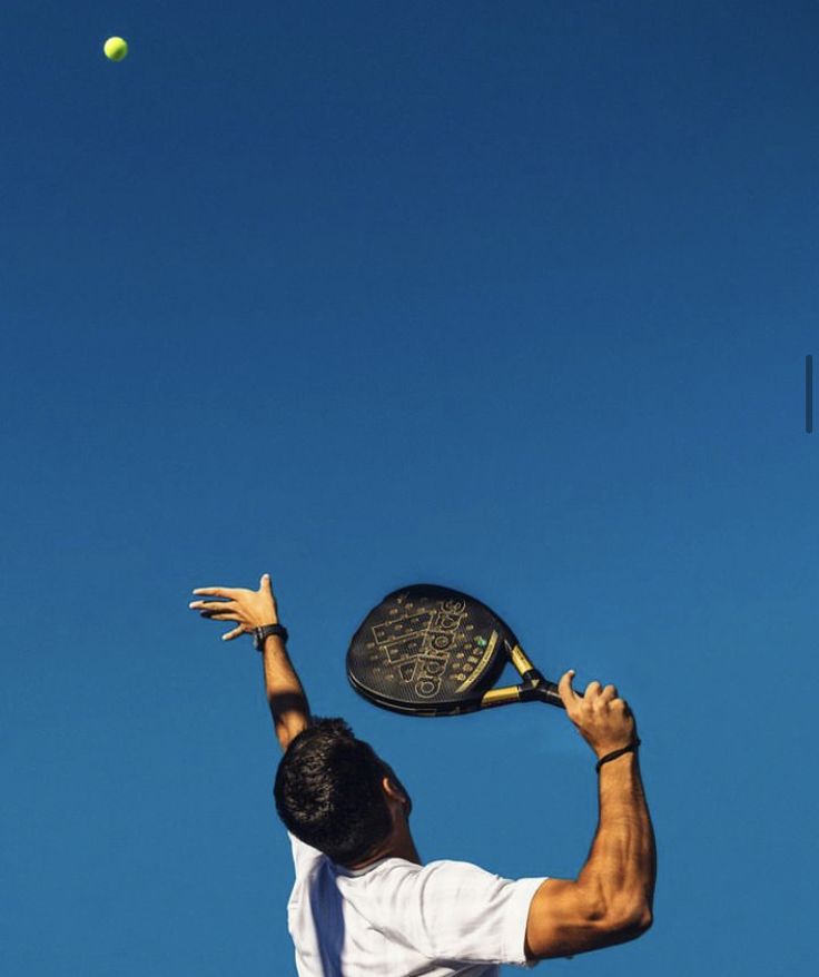 a man swinging a tennis racquet at a ball in the air on a sunny day