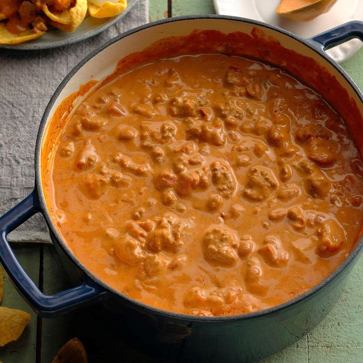 a blue pot filled with meatballs and sauce next to potato wedges on a table