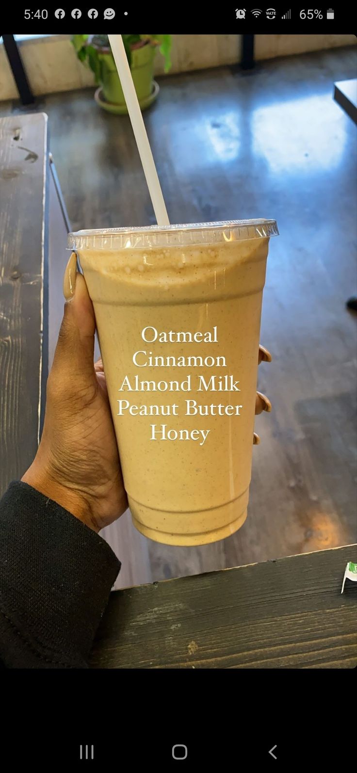 a person holding up a cup with a straw in it that says, oatmeal cinnamon almond milk and peanut butter honey