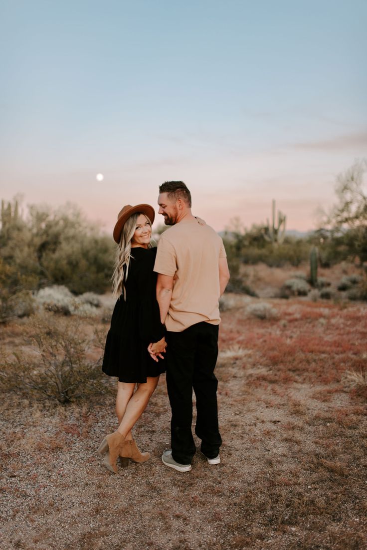 a man and woman standing in the desert at sunset with their arms around each other