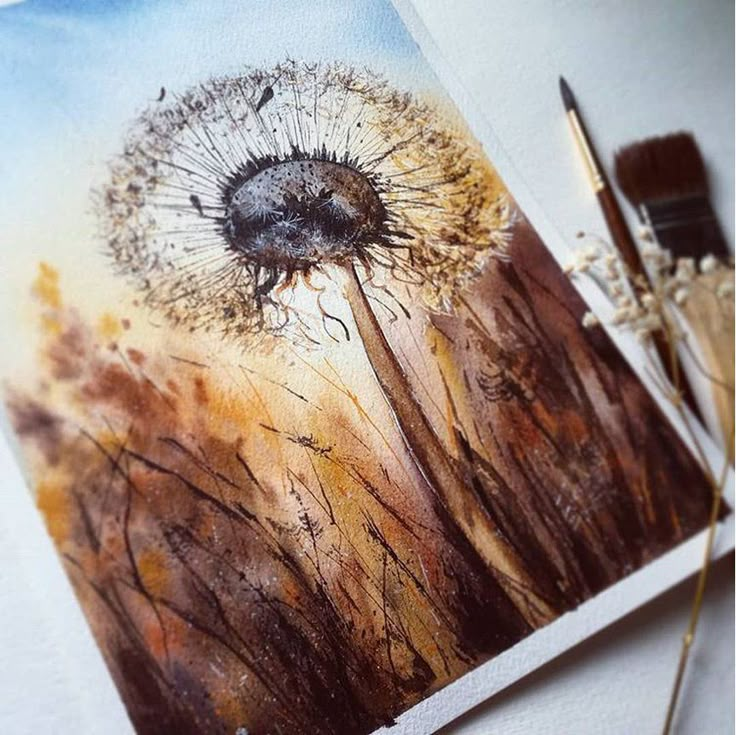 a watercolor painting of a dandelion on a piece of paper next to a brush