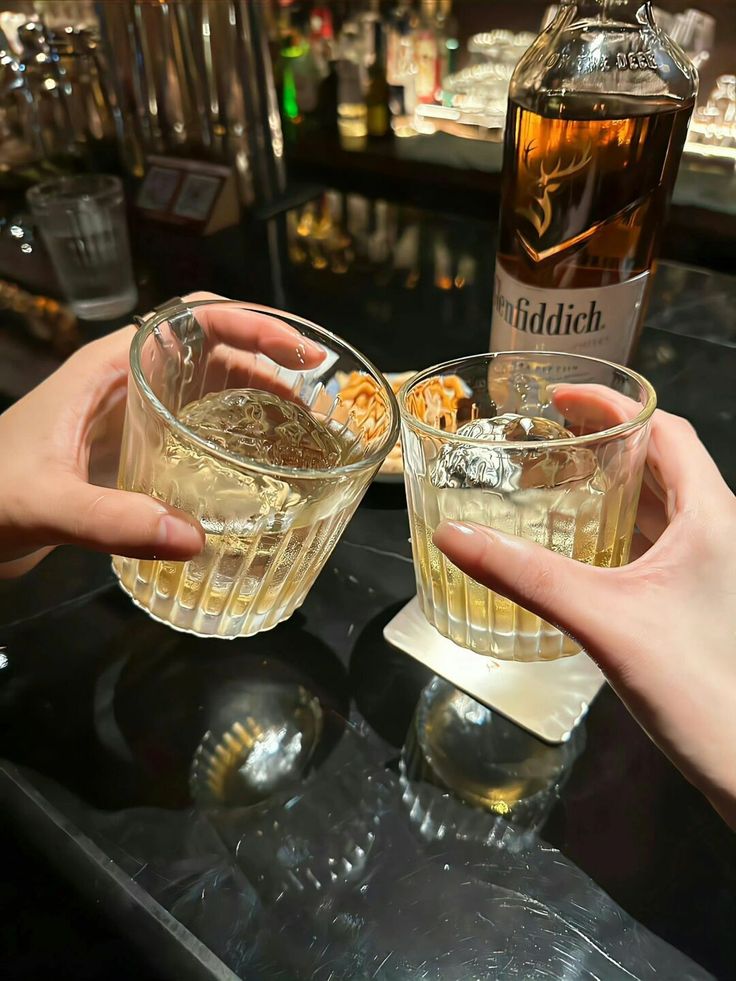 two people holding up glasses filled with alcohol