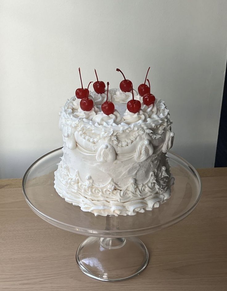 a cake with white frosting and cherries on top sitting on a glass platter