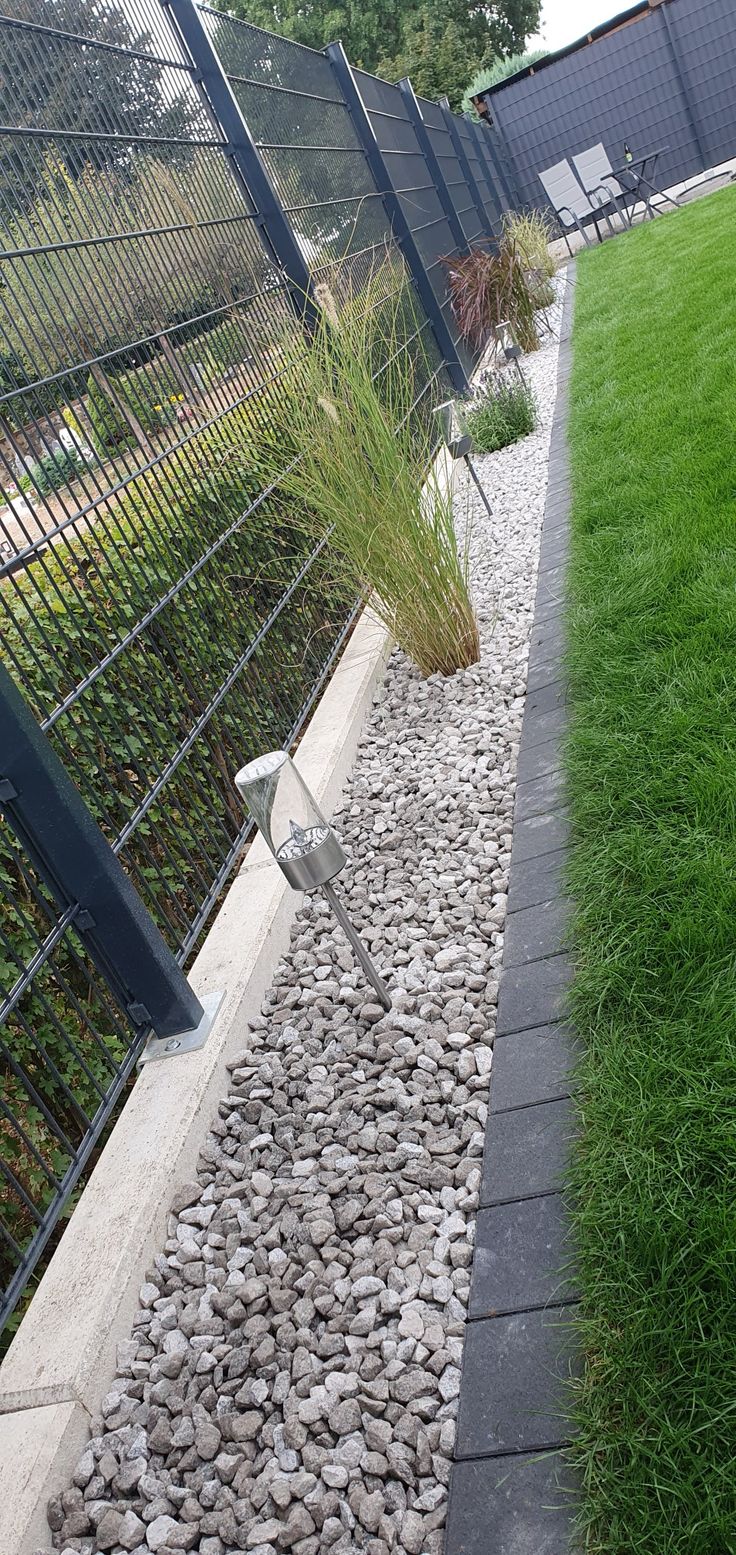 there is a bird that is standing in the grass by some rocks and gravel next to a fence