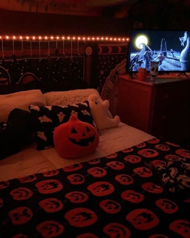 a bedroom decorated for halloween with pumpkins on the bed and a television in the corner