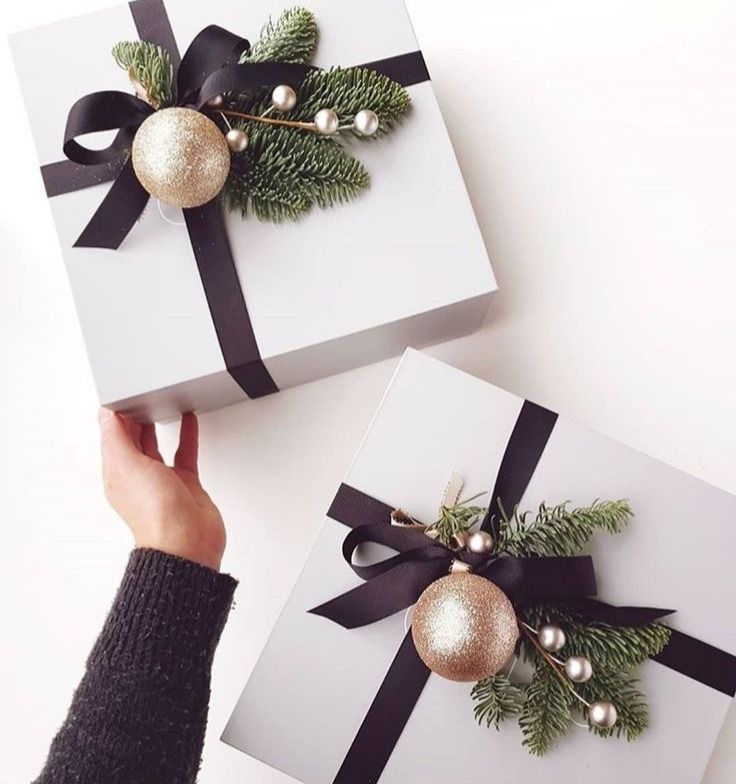 two white boxes with black bows and ornaments on them are being held by someone's hand