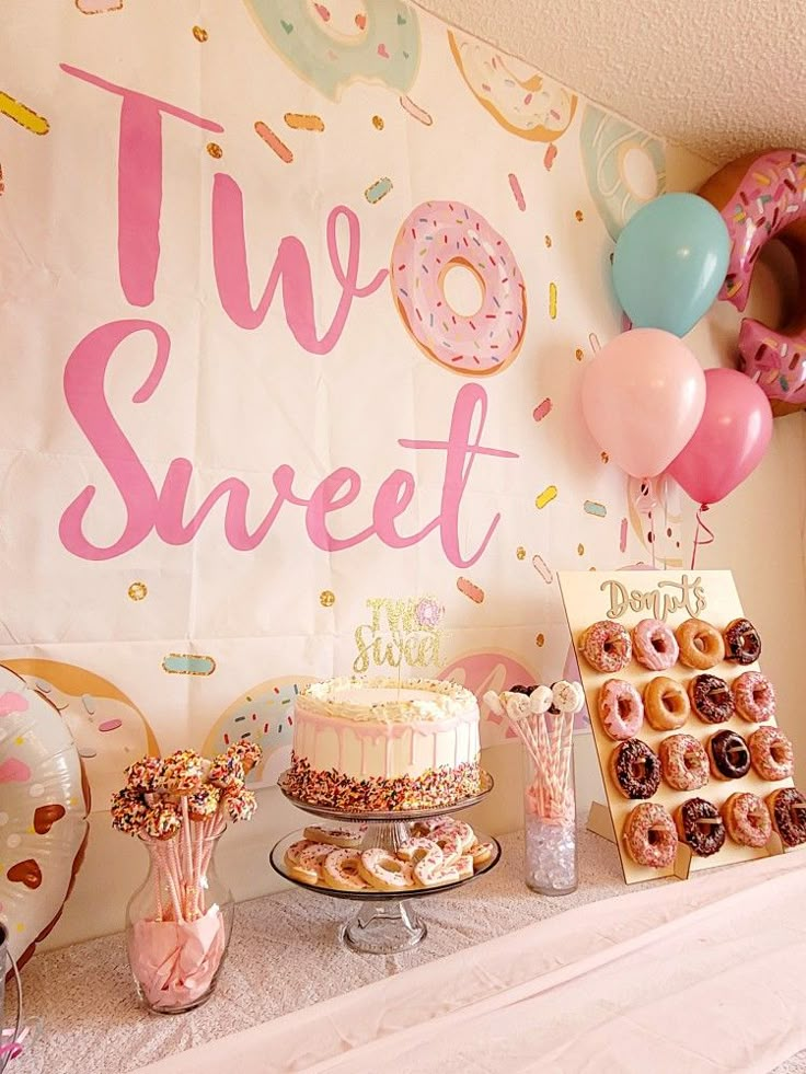 a table topped with cakes and donuts covered in frosting next to a sign that says two sweet