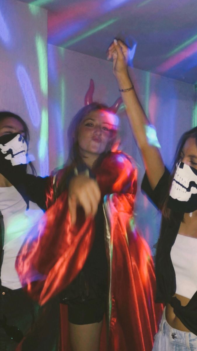 three women in costumes are dancing with their hands up and one is wearing a mask