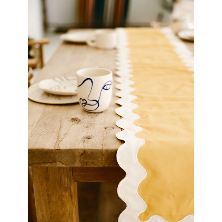 a wooden table topped with a white cup and saucer next to a yellow table cloth