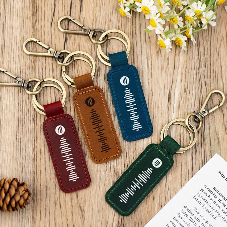 three leather keychains sitting on top of a wooden table next to a pine cone