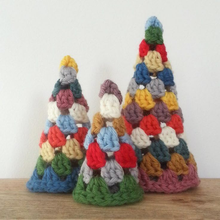 three small crocheted christmas trees sitting on top of a wooden table next to each other