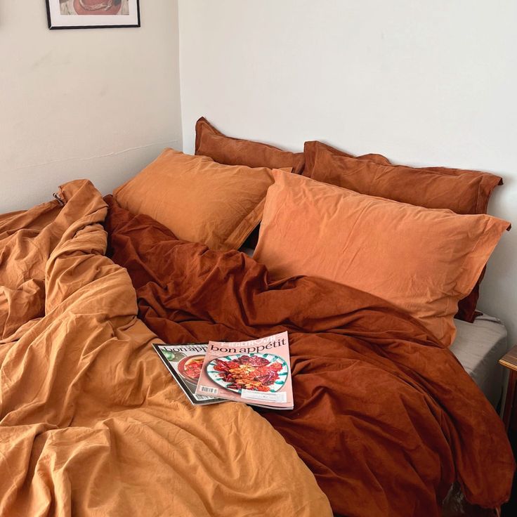 an unmade bed with orange sheets and pillows