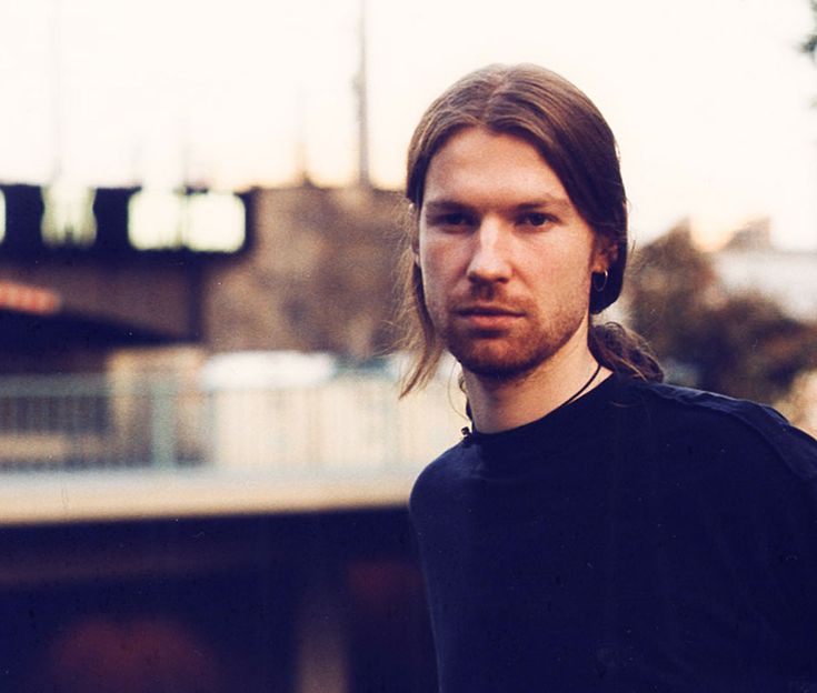 a man with long hair wearing a black t - shirt and looking at the camera