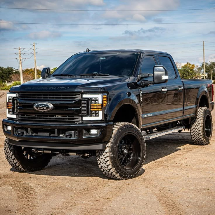 a large black truck parked on top of a dirt field