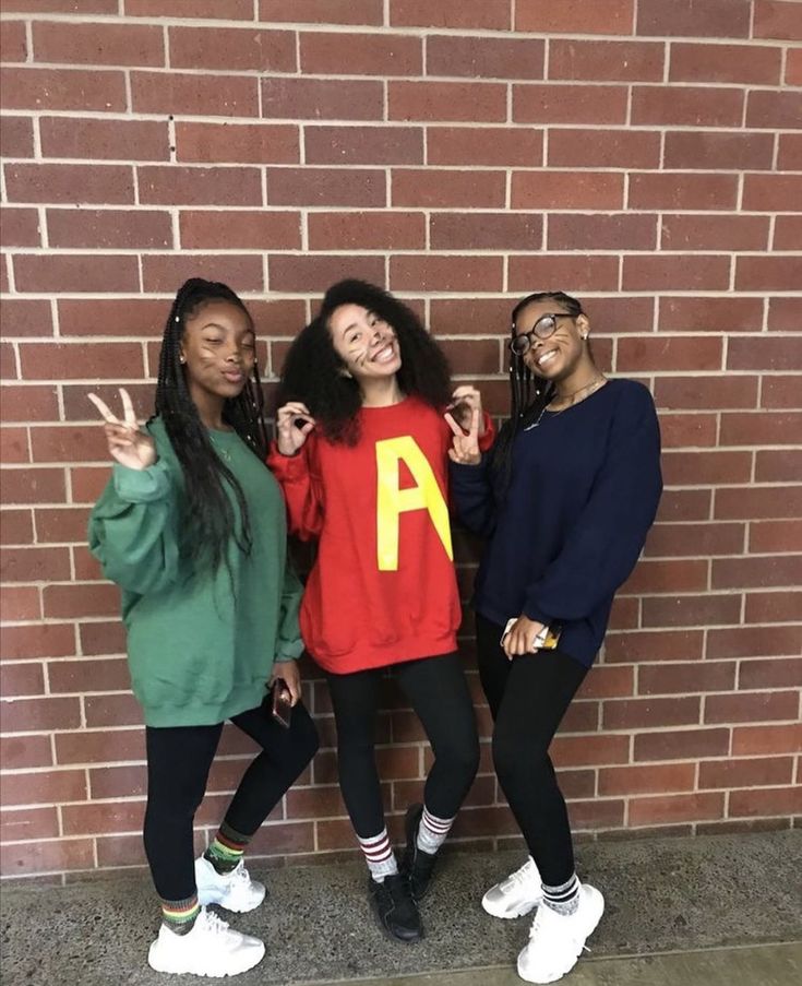 three young women posing in front of a brick wall with the letter a on it