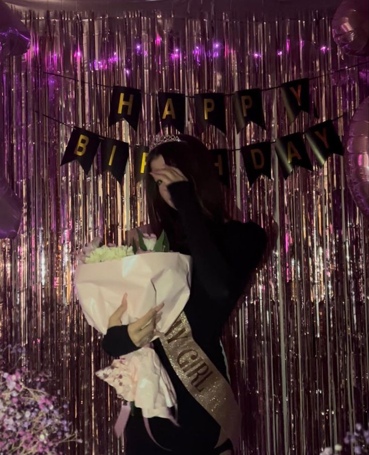 a woman holding a bouquet of flowers in front of a happy birthday sign and streamers