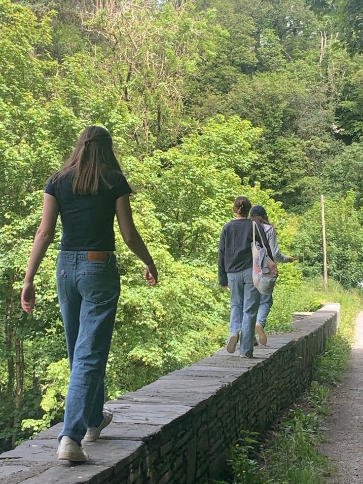 two people walking down a path in the woods with one person carrying a backpack on her back