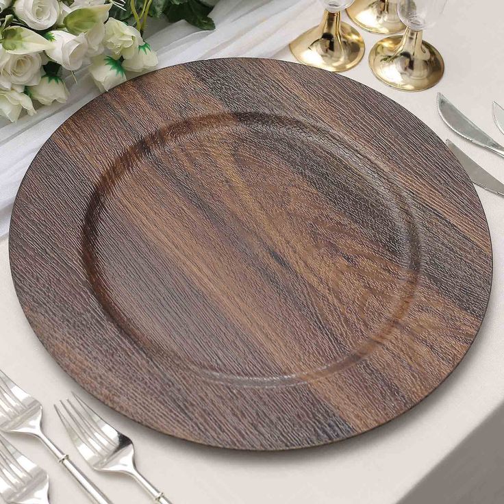 a wooden plate sitting on top of a table next to silverware and white flowers