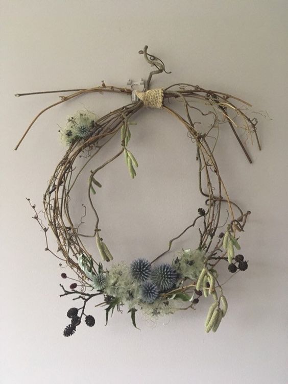 a wreath made out of branches and flowers hanging on the wall in front of a white wall