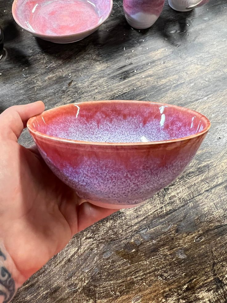 a hand holding a purple bowl on top of a wooden table next to other bowls