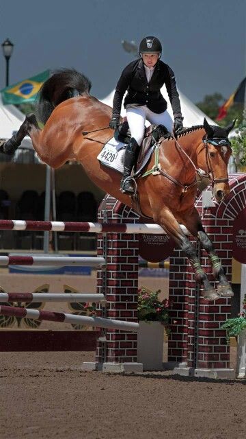 a woman riding on the back of a brown horse jumping over an obstacle with her legs in the air