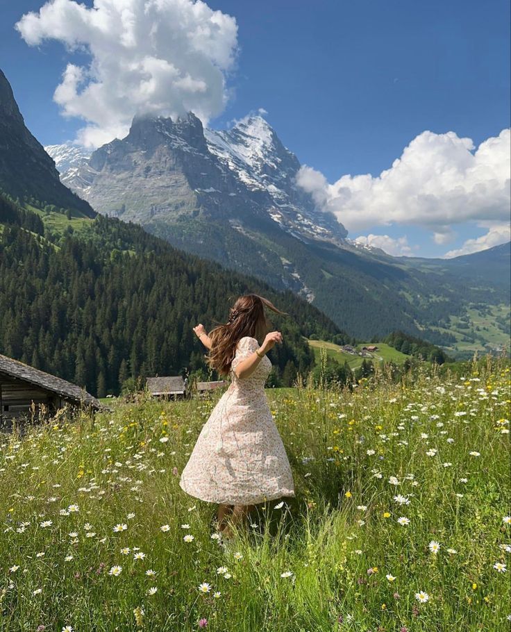 a woman in a dress standing on top of a lush green field next to a mountain